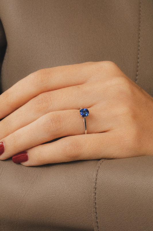 Photo zoomé sur une main portant une élégante bague en saphir bleu. Le design épuré de l'anneau sublime la beauté naturelle de la pierre centrale sertie en 4 griffes.