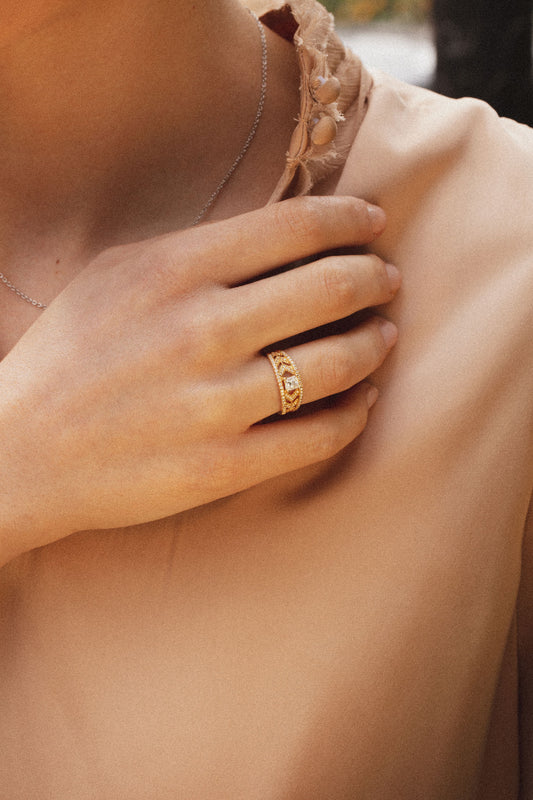 Photo d'une femme habillée d'une jolie blouse en satin rose poudré. Elle porte à son doigt une bague ajourée en or jaune 18 carats. Son ajourage apporte modernité et lumière à l'ensemble de la création. Elle reflète une personnalité audacieuse.