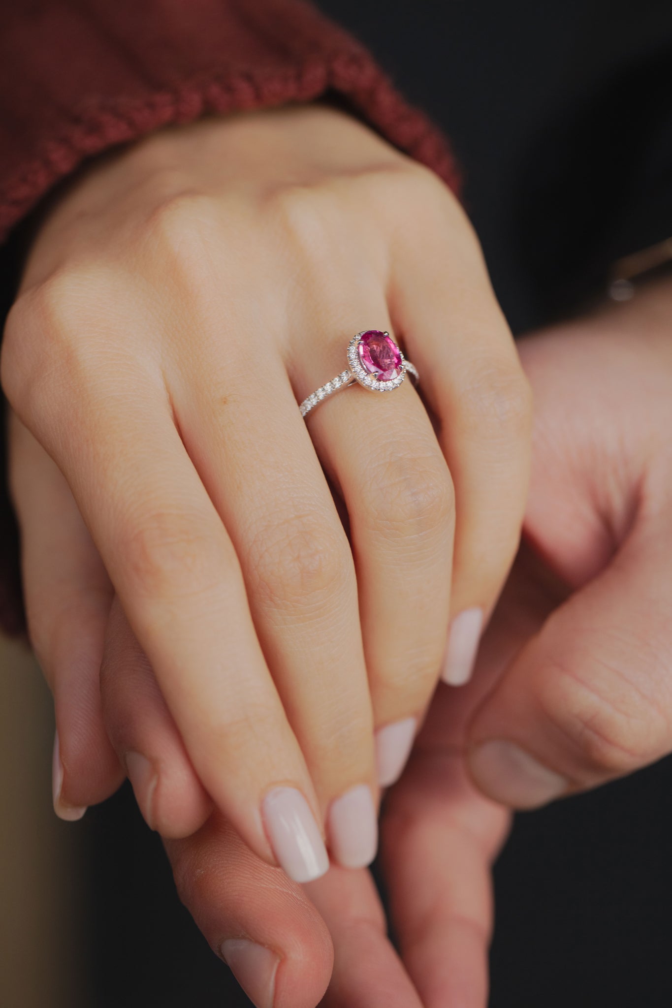 Photo d'une main de femme portant le solitaire Pivoine accompagné et avec halo, saphir rose, diamants et or blanc 18 carats.