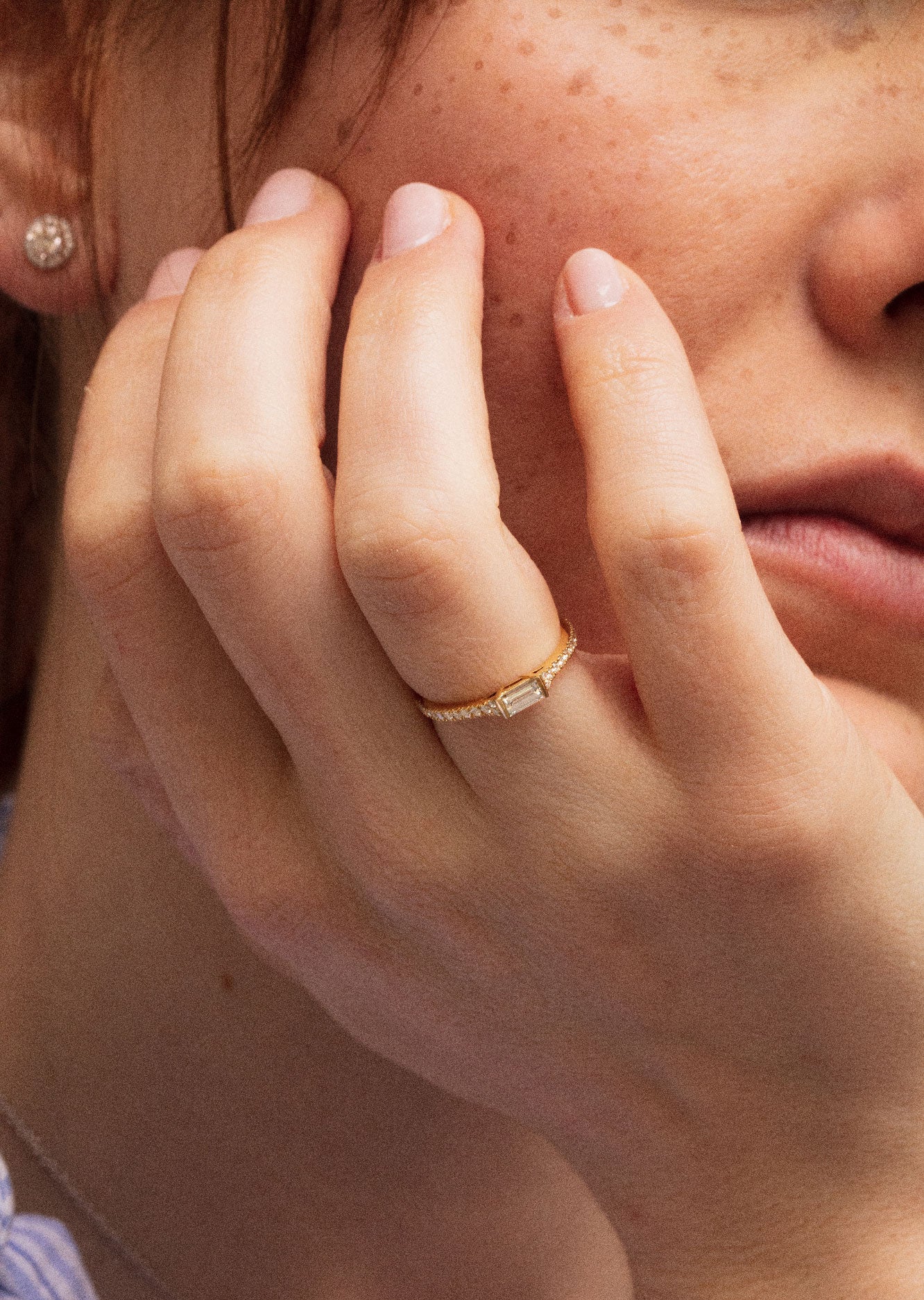 Photo close-up d'une femme portant des bijoux. La bague en or jaune est pavée de diamants éclatantes. On distingue à son oreille une boucle d'oreille en forme ronde.