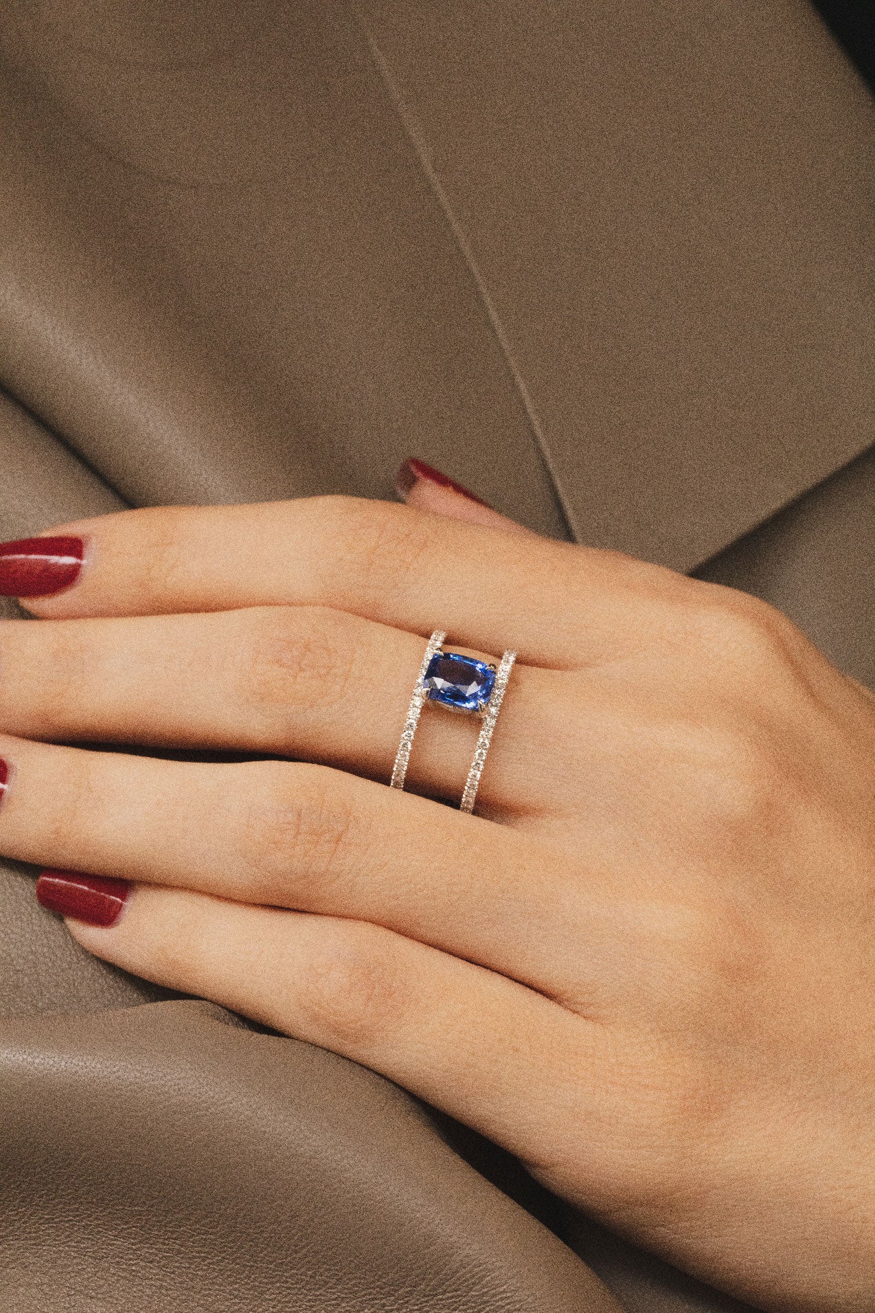 Photo d'une main de femme portant une splendide bague en saphir bleu. La pierre précieuse centrale est magnifiquement encadrée par deux rangées de diamants scintillants.