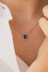 Photo zoomé d'une femme portant un collier en saphir bleu entouré d'un délicat halo en diamants. 