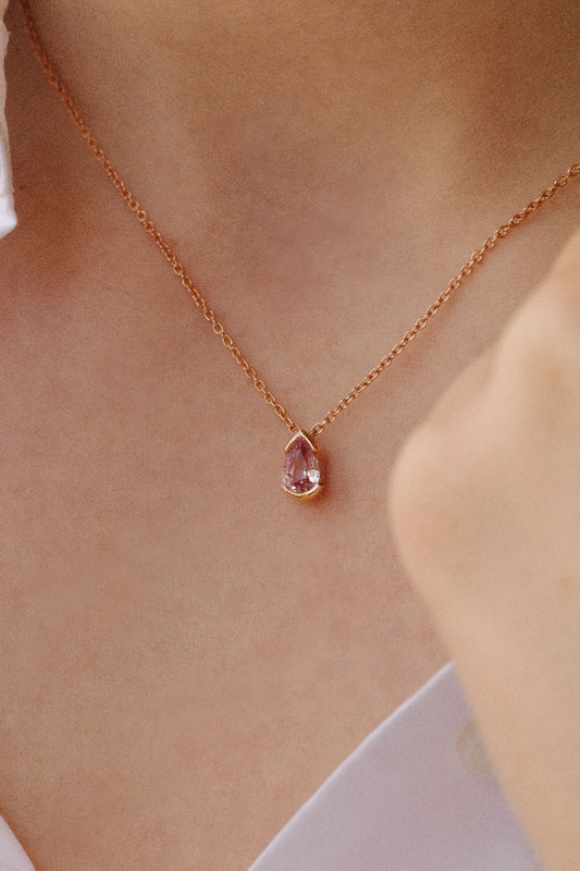 Photo porté d'un collier en or rose orné d'un pendentif en forme de goutte. La pierre centrale est un saphir rose.