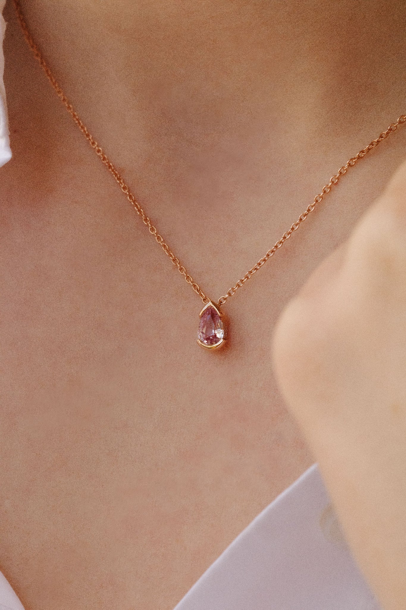 Photo porté d'un collier en or rose orné d'un pendentif en forme de goutte. La pierre centrale est un saphir rose.