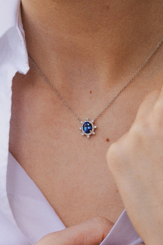 Photo zoomé sur le cou d'une femme. Elle porte un délicat collier en saphir bleu entouré d'un éblouissant halo de diamants.