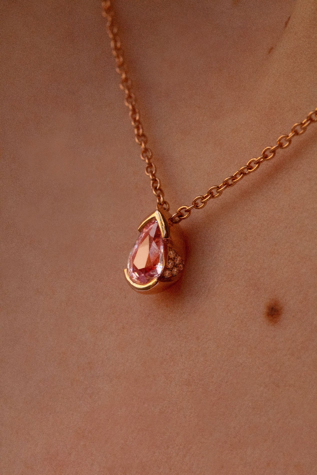 Photo zoomé sur les détails minutieux du collier en saphir rose. Des délicats diamants brillants ornent les bords latéraux du pendentif.