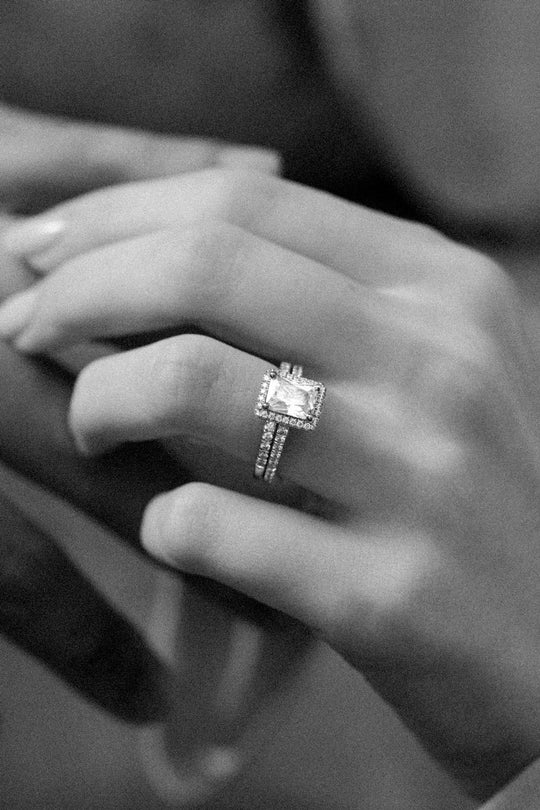 Photo en noir et blanc d'une main de femme portant un duo de bagues de fiançailles et de mariage en or 18 carats